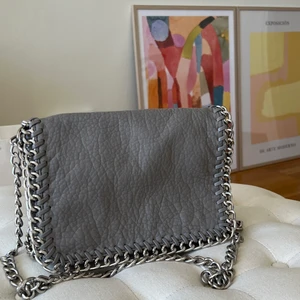 Tiamo Väska  - Säljer min väska från märket Tiamo, i färgen grå. I bra skick förutom att färgen på dragkedjan av väskan lossnat på vissa ställen, även mörkare baktill. 