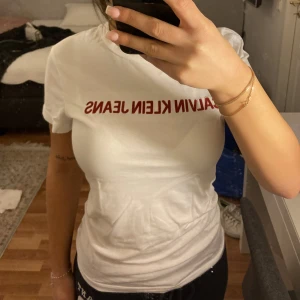 T-Shirt - Calvin Klein - Calvin Klein tröja utan anmärkningar. Jättefin tröja i stl XS som passar till allt. Tröjan är vit med röd broderad text. Säljer pga att det inte längre är min stil😊