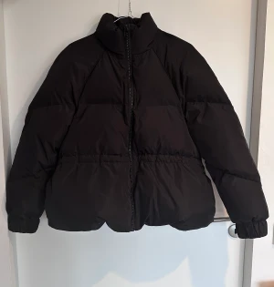 Ganni witham puffer Jacket strl M svart - Strl M. True to Size. En riktigt fin svart dunjacka, bombermodell och med dragsko i midjan för att kunna justera en timglas silhuett om man vill, med ett vattenavvisande skal. Den har knappt blivit använd och nyskick. 100% polyester. Ord 4500 kr
