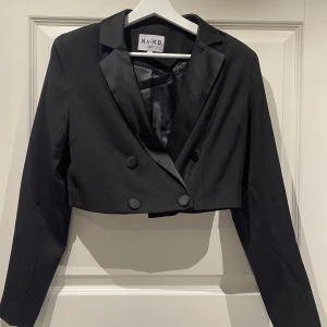 Svart Croppad Blazer - Säljer nu denna favoriten, en svart croppad blazer med axel muddar i storlek 38. Inköpt från NA-KD för 599kr säljs nu för 199kr. Fraktas på köparens bekostnad 