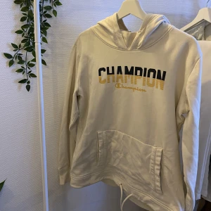 Champion hoodie - Jättefin beige hoodie från Champion. Med ett tryck som är guld o svart på framsidan. Går att dra in längst ner för en annorlunda passform. Som ny:)
