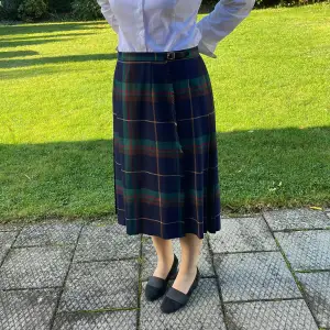 Tartarmönstrad skotsk kjol i ren skotsk ull. Blå och grön med bruna, gula och röda inslag. gMidjemått 88-90 cm. Går att justera.Längd : 70 cm. 