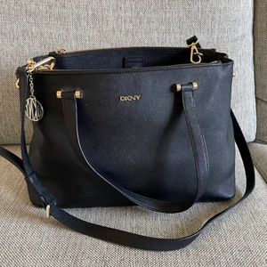 DKNY väska - Säljer min DKNY-väska i svart, äkta läder. Nypris: 3200kr Mått: 36x17x25 Skick: Väldigt bra, använt skick  Förutom huvudfacket i väskan finns två stora fack i vardera sida. I väskan får även laptops plats då väskan är väldigt rymlig. 