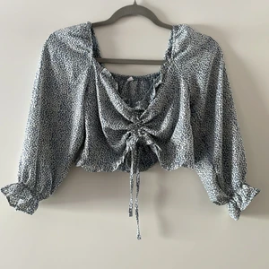 Blå, prickig blus - En blå blus med vita prickar. Band i mitten som man drar åt själv. Dragkedja i sidan.