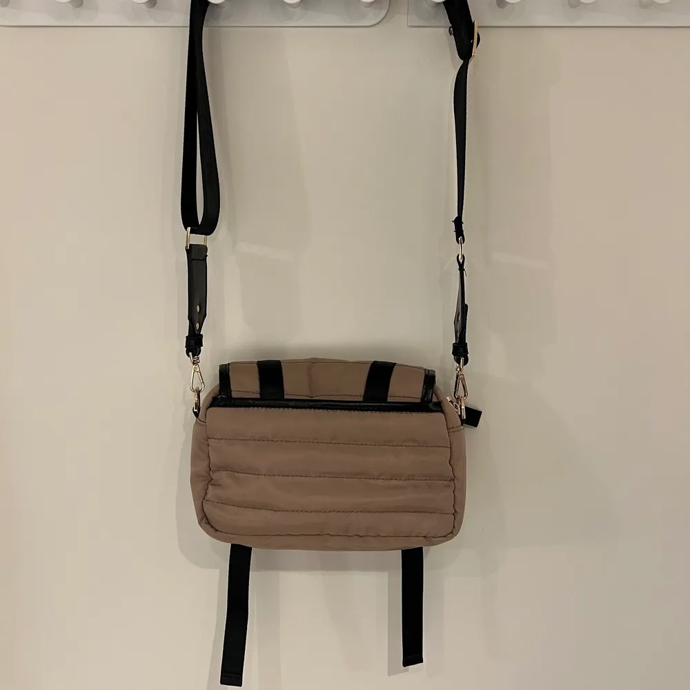 Olympia crossbody bag från Ideal of Sweden. Beige med svarta och ”guld” detaljer. Har dragkedja och två spännen på baksidan. Öppet fack på baksidan. Använd fåtal gånger och har inga defekter, är som ny. Nypris 999 kr . Accessoarer.