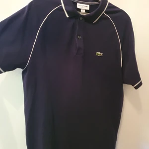 Marinblå Lacostepiké - Marinblå Lacostepiké med vita detaljer. Tre år gammal, använd fyra gånger och i mycket gott skick. Nypris 89 euro