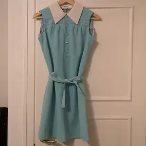 Turkos vintageklänning från 60-talet. Fin krage, knappar och broderade detaljer. Kan användas med eller utan skärpet. Klänningen slutar strax över knäna och är i en rak modell. Använd men i gott skick! Passar storlek XS-S. 