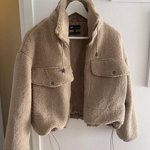 Teddy (crop) jacka  - En beige Teddy crop jacka i storlek M. Det går att tajta till jackan där nere med två snören, lika så kragen. Finns dragkedja och två fickor. Använd ca 6 gånger så den är som nyskick.