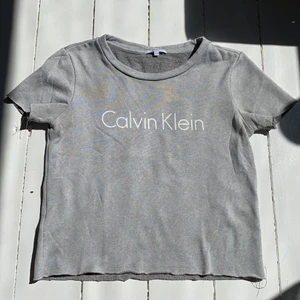 Calvin Klein t-shirt - Grå t-shirt med tryck från Calvin Klein. Storlek 12-14 men sitter som XXS. Tröjan är lite croppad (var så när man köpte den, har nt gjort själv) så man behöver inte vika upp eller stoppa ned den i byxorna. Super bra skick förutom att tråden ”fransat” sig lite. Säljer pga att plagget nt kmr t användning längre 🖤