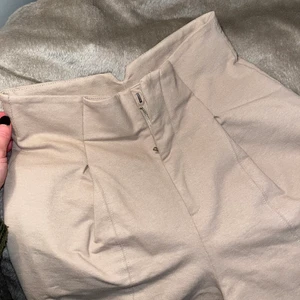 Kostymbyxa - Ljust beige kostymbyxa från H&M. Ankellånga med en ca 2cm slits fram till. Pressveck vid höften och hög midja. Otroligt sköna, dock inga fickor