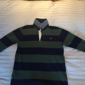 Gant tröja  - Ganttröjan är långärmad med krage. Den är använd men i bra skick. Färgen är mörkblå och mörkgrön. Storleken är 158/164.