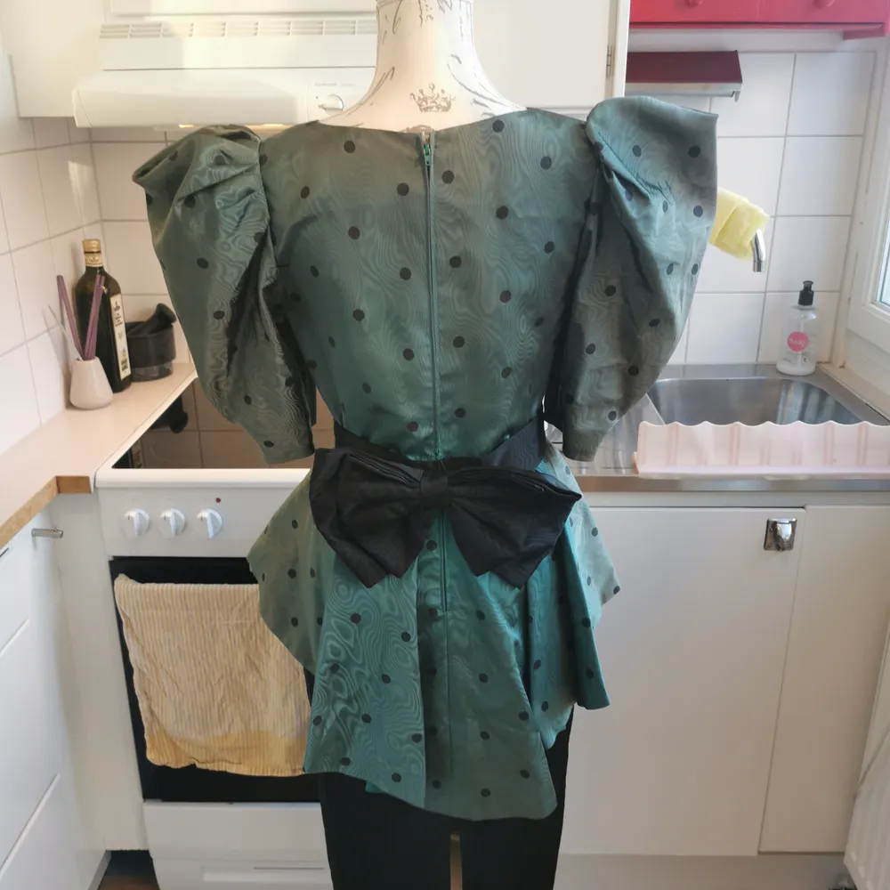 One of a kind vintageklänning tillverkad i Frankrike. I fint skick med svarta pricka på skimrande grönt och en svart rosett vid ryggslutet. 70cm i omkrets runt midjan. . Klänningar.
