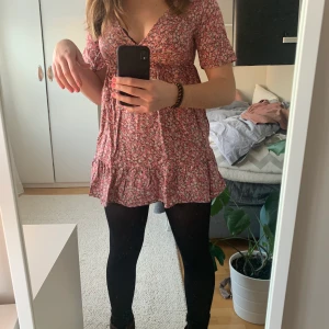 Blommig klänning - Söt blommig klänning från Pull&Bear! Klänningen är v-ringad upptil med snörer man kan knyta under bysten. Jättefin sommarklänning eller om man ska utomlands men kan även stylas med strumpbyxor för en mer vintrig look! Kontakta mig om du är intresserad eller för mer info☺️