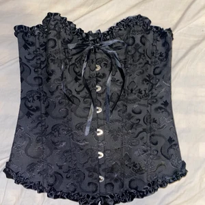 Svart korsett - Svart korsett från Lightinthebox, perfekt nu till halloween men även vid andra tillfällen. Enbart testad, nyskick. Stoleken varierar lite beroende på hur mycket man är villig att dra åt den. Sista bilden är från hemsidan, där syns de hur den ska sitta. Köp direkt för 130kr exkl. frakt.