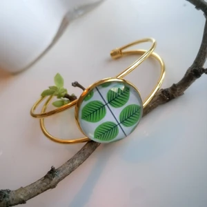 Guldfärgat armband motiv Berså - Guldfärgat stelt armband som är justerbart. I guldfärgad metall samt glas, med motiv av "Berså" från Rörstrand. Motivet är 25 mm i diameter. 