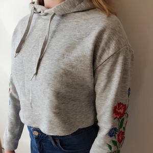 Croppad hoodie  - Grå croppad hoodie med broderade blommor på ärmarna. Super fin och söt, men inte riktigt min stil. Bra skick!