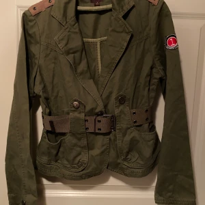 Jacka i kort modell - Snygg midjejacka med skärp. Köpt i London för ett par år sedan. Kakigrön. Märkt med storlek L men den känns liten. Jag har XS