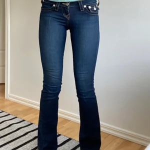 True Religion lådmidjade bootcut jeans  - Coola lågmidjade bootcut jeans från True Religion med en mörkare ton, storlek 23 som passar perfekt på mig och jag är 174 cm. Innerbenslängden är ca 83 cm och midjemåttet ca 73 cm! Inte säker att jag vill sälja så kom med bra bud💕Köparen står för eventuell frakt