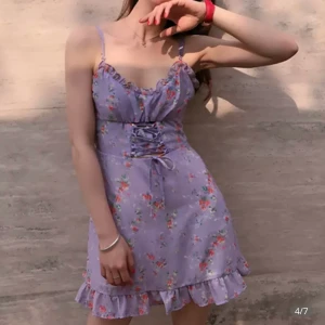 Söt blommig klänning - Lila klänning med blommor på och snöre i mitten så man kan göra den lite taightare runt midjan. Den är väldigt lätt och sval för sommaren. Det står att den är storlek s men jag skulle säga att den även passar om du har storlek xs.