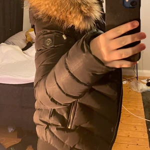 HOLLIES Stockholm jacka - Jackan är i modellen chantel och har guld detaljer. Storlek 36. Jackan är köpt vinter 2019 och bara använd 1 säsong. Väldigt fräsch i skicket överlag, finns en ljusare fläck på höger sida frampå men ingenting som syns direkt. Pälsen på luvan är äkta. Säljer för att jackan är för liten och inte används längre. Betalas via Swish. Vid intresse av fler bilder, skicka pm till mig.                             