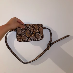 Åhléns snake midjeväska - Detta är en midjeväska från Åhléns i ormskinn mönster. Det som är bra med denna är att det också är ett skärp som gör att väskan sitter fast i byxorna hela tiden. 