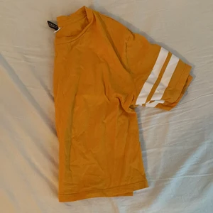 Orange T-shirt Från H&M  - Plagget har använts en gång för en tävling och har sedan dess inte används, tröjan är till navel längd. Den orange färgen är stark och syns väldigt bra 