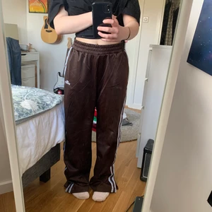 Bruna H&M byxor stl. M - Ett par bruna ”tracksiut” byxor från H&M i storlek M. Byxorna har blåa och vita ränder längst sidorna på byxbenen och dragkedja längst ner vid anklarna. Dessa byxorna köpte jag för ett tag sedan men använder de aldrig då de är för stora/långa. Hade jag köpt de i en mindre storlek hade jag älskat dem eftersom de är så jäkla snyggaoch bekväma!! De sitter löst runt benen men är tajtare i midjan. Jag tror att du som är lite längre hade älskat dessa byxor! 🥰🥰 Kan mötas i Karlskrona annars 30kr frakt❤️