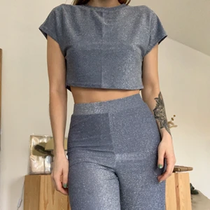 Glittrigt set Hannalicious - Glittrigt set från Hannalicious kollektion med NA-KD. Croppad t-shirt och vida byxor. Blågrå i färgen, sista bilden är mest rättvis. Skönt och stretchigt så passar allt från XS-M. Använt fåtal gånger, som nyskick 💙