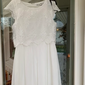 Studentklänning i nyskick  - Vit kort klänning med spets upp till, både i bak och fram. 100% polyester. Är i nyskick, använde den inte på studenten. Prislappen sitter fortfarande kvar. KÖPAREN STÅR FÖR FRAKTEN!