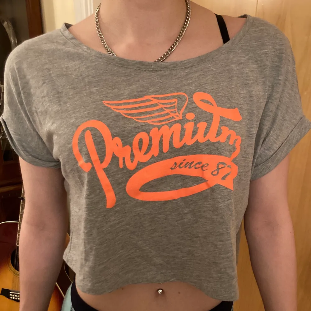 A gray crop top t-shirt with neon orange text dom säger premium since 1887. Använt ett par gånger. . T-shirts.