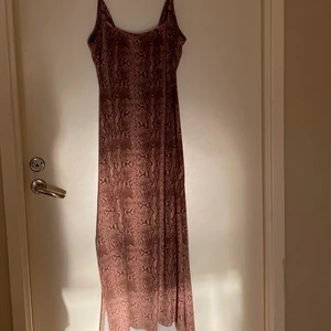 Ormmönstrad brun långklänning. - Urringad klänning i runt mönster och slits vid sidan. Den har justerbara band. 