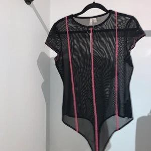 Body i mesh med rosa detaljer storlek 42 (Passar M-L) - Oanvänd t-shirt body i mesh! Har endast testats, lappen kvar. Supersnygg på och till fest, säljer då det inte är min stil längre. 