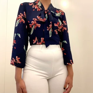 Marinblå blus med blommor  - Marinblå blus med blommor och vida ärmar. Knytning runt halsen som man själv kan knyta. Trekvarts långa ärmar. Storlek XS. 