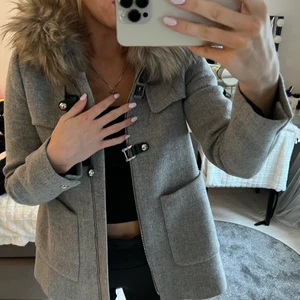 Grå kappa med päls - Grå jacka med päls på luvan, har knäppen och en dragkedja