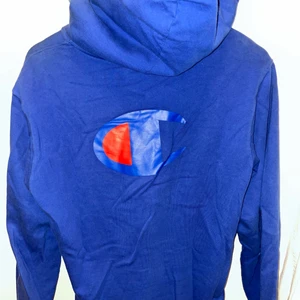 Champion Hoodie - Blå champion hoodie, med stor C logga på ryggen, liten logga på högra bröstet och Champion logga/text längs höra armen. Lite upphöjd krage. I bra skick. frakt tillkommer