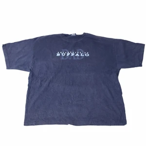 University At Buffalo - Graphic Tee  - En riktigt Nice Mörkblå tröja som är sjukt nittiotalsaktig, den kan vara från nittiotalet men vi vet inte med 100% säkerhet om den är det. Har ett tryck i mitten och kommer från universitet i Buffalo. Trycket har en fin ljusblå färg.