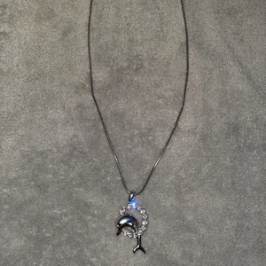 Halsband - Ett väldigt fint halsband med en liten delfin som halft hoppar ur en ring, prefekt present för ett yngre sykon. Köparen står för frakt