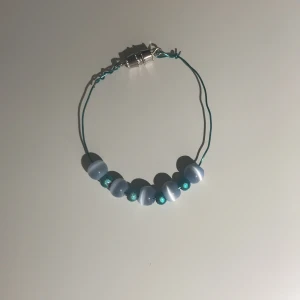 Blått hemgjort armband - Armband gjort i blå ståltråd med pärlor, ca 14 cm långt. 15 kr inklusive frakt