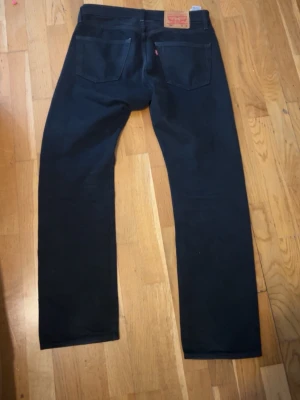 Svarta Levi's jeans  - Snygga svarta jeans från Levi's med klassisk femficksdesign och raka ben. Jeansen har en läderpatch bak i midjan och är tillverkade i ett slitstarkt bomullstyg. Perfekta för en stilren och tidlös look.