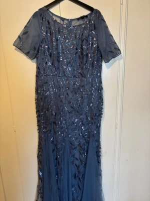 Mörkblå långklänning med paljetter - Elegant mörkblå långklänning med korta ärmar och glittriga paljettdetaljer i ett mönster över hela klänningen. Knappt använd  och har  en lätt transparent mesh upptill o