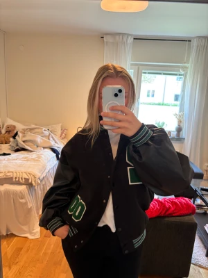 Svart och grön bomberjacka varsitystil - Säljer en cool oversized svart jacka med streetwear 90-tals känsla, jättesnygg men kommer tyvärr inte till användning