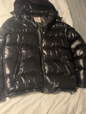 Svart glansig dunjacka från Moncler - Snygg svart dunjacka från Moncler med glansig finish och huva. Jackan har två dragkedjefickor framtill och klassisk Moncler-serietidningsetikett på insidan. Perfekt för kalla vinterdagar och riktigt trendig look. Kvitto går även och lösa,pris kan diskuteras vid snabb affär hör av er vid frågor.//Love
