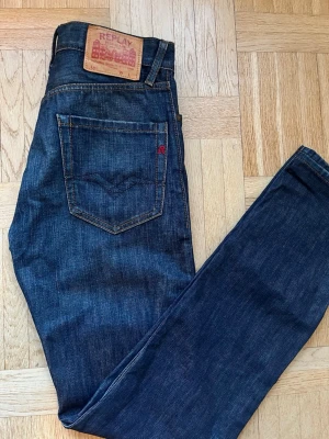 Mörkblå jeans från Replay - Snygga mörkblå jeans från Replay med klassisk femficksdesign och raka ben. Jeansen har en läderpatch med Replay-logga bak i midjan och kontrastsömmar. Perfekta för dig som gillar en tidlös och stilren look.