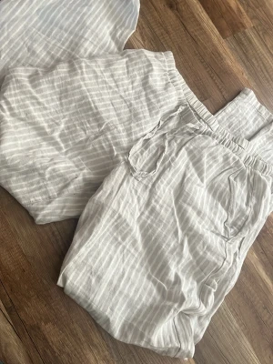 Randiga vita linnebyxor - Luftiga linnebyxor i vitt med tunna vertikala ränder. Byxorna har resår i midjan och sidofickor, vilket gör dem både bekväma och stilrena. Perfekta för en avslappnad och trendig look. Materialet är mjukt och svalt linne.