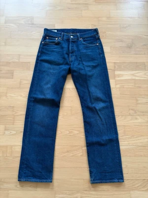 Levi's raka blå jeans - Klassiska blå jeans från Levi's med rak passform och fem fickor. Jeansen har en djup indigo färg, kontrastsömmar och läderpatch bak i midjan. Tillverkade i slitstark denim, perfekta för en avslappnad och tidlös stil.