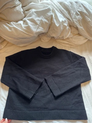 Svart basic stickad tröja - En enkel svart stickad tröja med rund halsringning och ribbade muddar vid ärmslut och nederkant. Perfekt för lager på lager och passar till det mesta. Klassisk rak passform och mjukt material. Sitter perfekt på mig som bär S 