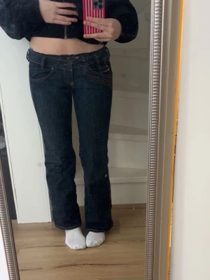 Mörkblå bootcut jeans från diesel industry  - Mörkblå bootcut jeans med snygga kontrastsömmar och detaljerade fickor både fram och bak. Jeansen har låg midja och klassisk femficksdesign. Perfekta för en trendig och avslappnad look. Jag har storlek 36 på byxor och dessa passar mig helt okej lite korta, jag är 167cm