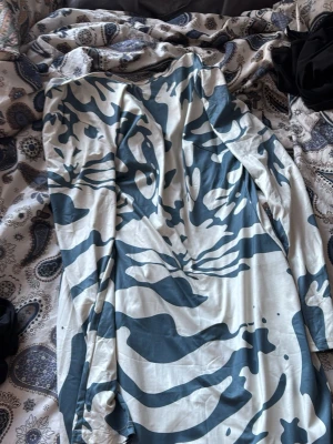 Vit och blå långärmad klänning - Säljer en långärmad klänning med vit bas och blått kamouflagemönster. Klänningen har v-ringning och är i ett mjukt, stretchigt material som känns bekvämt mot huden. Perfekt för dig som gillar unika mönster och vill sticka ut.