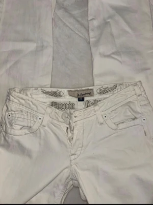 Vita jeans från J & company  - Snygga vita jeans från J & Comapny med raka ben och coola detaljer på bakfickan, inklusive broderi och nitar med låg midja. Innersbenlängd 82cm 
