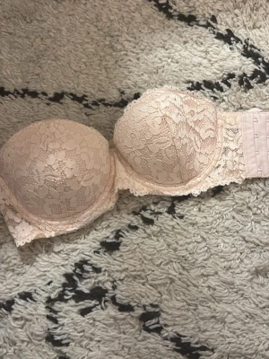 Ljusrosa spets-bh utan axelband, men man kan sätta ditt egna axelband. Storlek 70 A. Alldeles för liten för mig. - Säljer en ljusrosa bh med vadderade kupor och vacker spets över hela bh:n. Bh:n är utan axelband och har silikonkanter för extra stöd samt hakknäppning bak. Perfekt för toppar utan axelband och ger en snygg siluett. Man kan sätta på egna axelband.